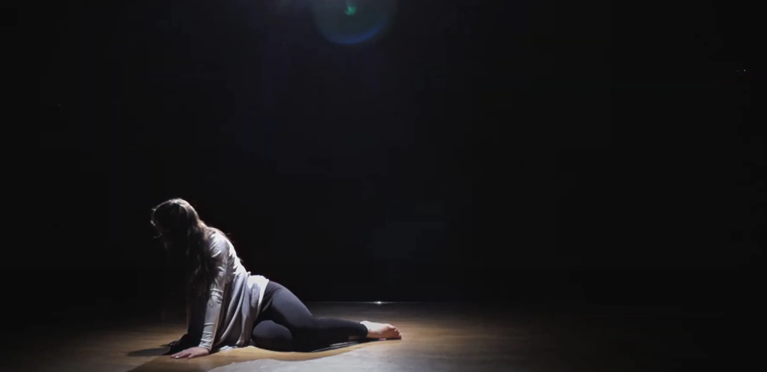 An actress in spotlight, lying defeated on a stage.